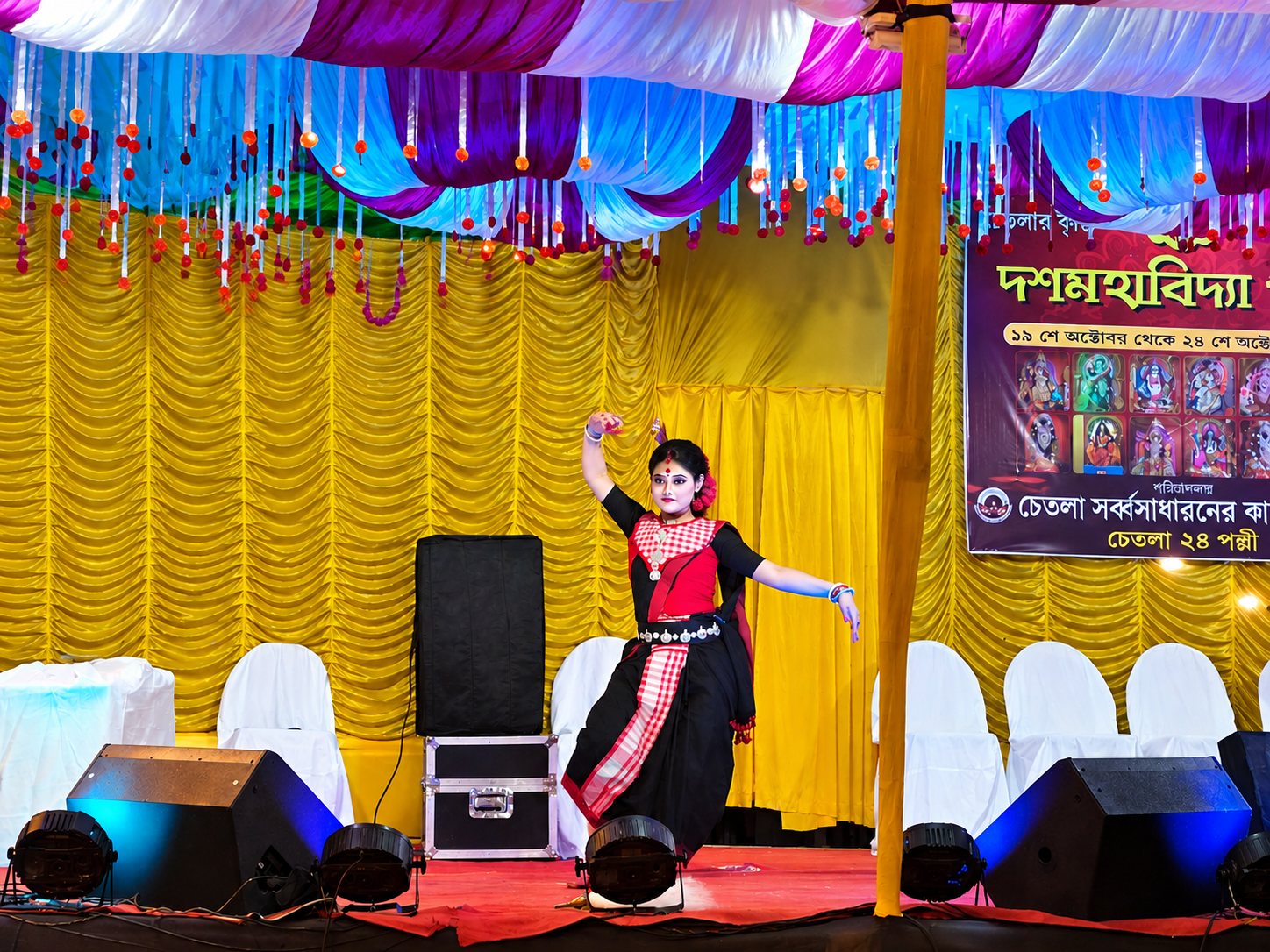 A classical dancer performing on the Dasamahavidya Puja stage in Chetla, with the celebration banner behind