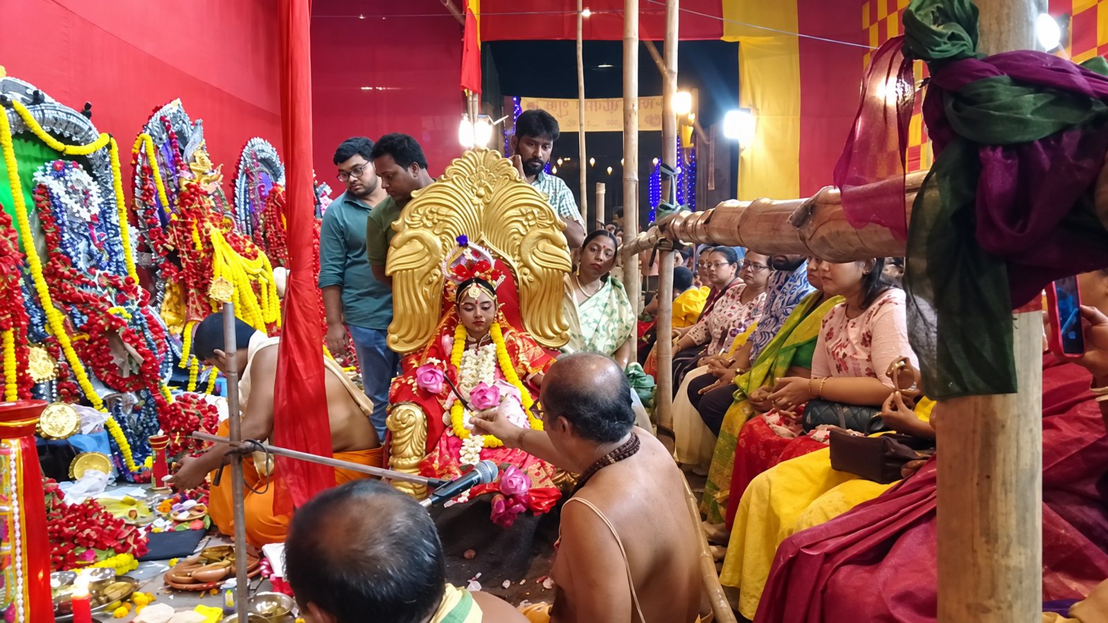 Kumari Puja during the night-long Dasamahavidya observance — the young Kumari seated on the golden throne as the priest offers worship, with the Mahavidyas behind