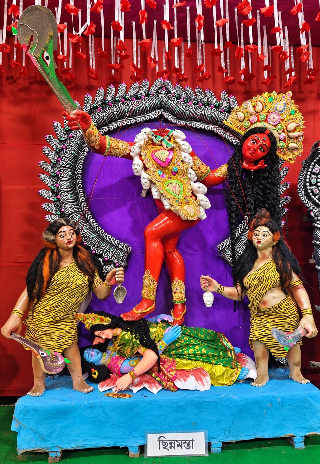 Maa Chhinnamasta — the crimson Goddess holding her own head and the scimitar, flanked by her two attendants, with her nameplate 'ছিন্নমস্তা' below