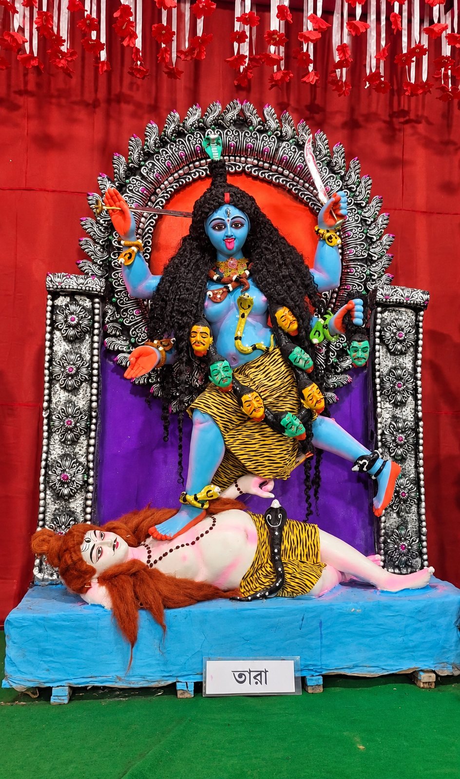 Maa Tara — the blue Goddess standing upon the reclining Shiva, wearing a tiger skin and a garland of heads, her nameplate 'তারা' below