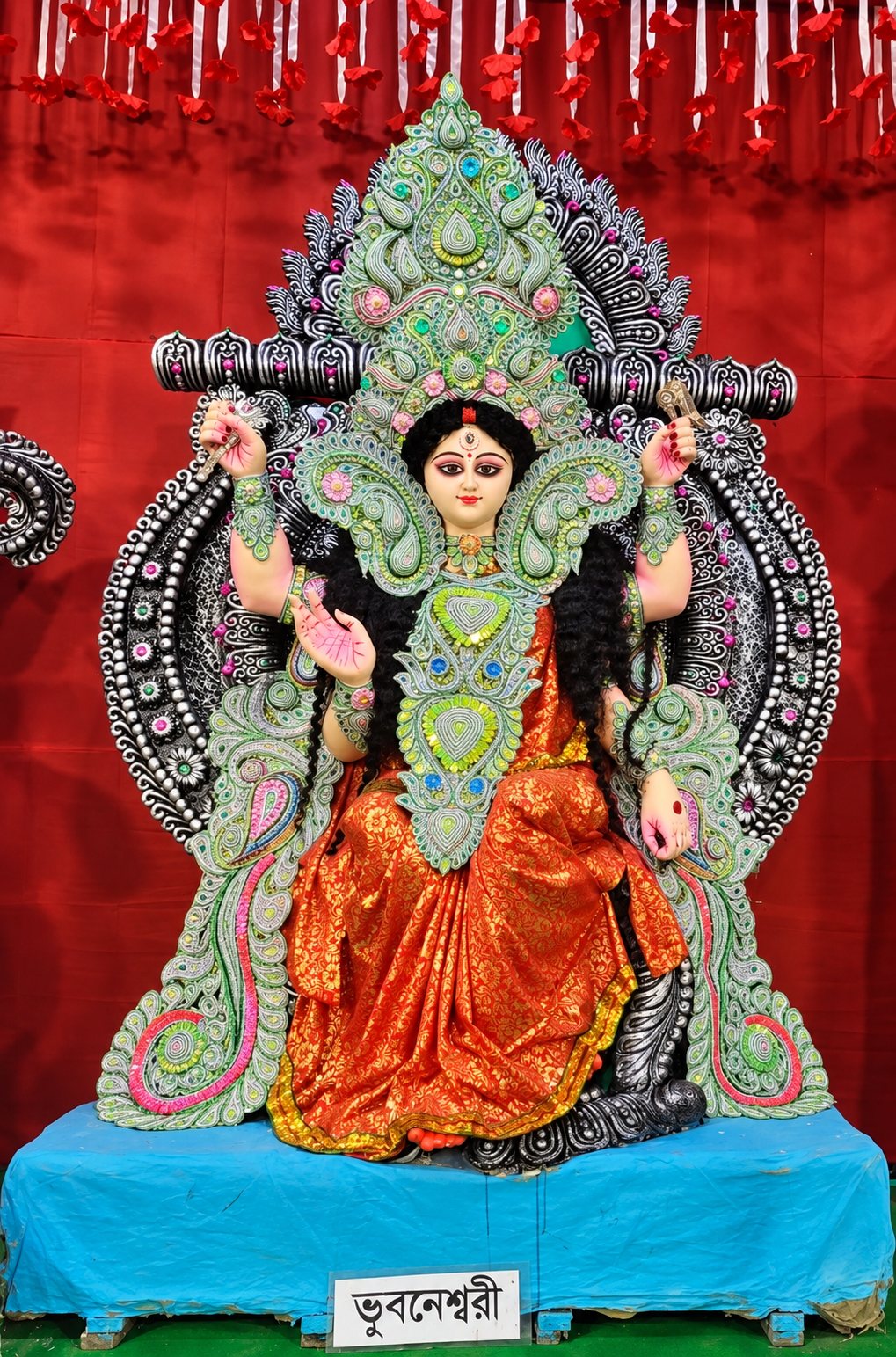 Maa Bhuvaneshwari enthroned in orange and green, four-armed, with her nameplate 'ভুবনেশ্বরী' below